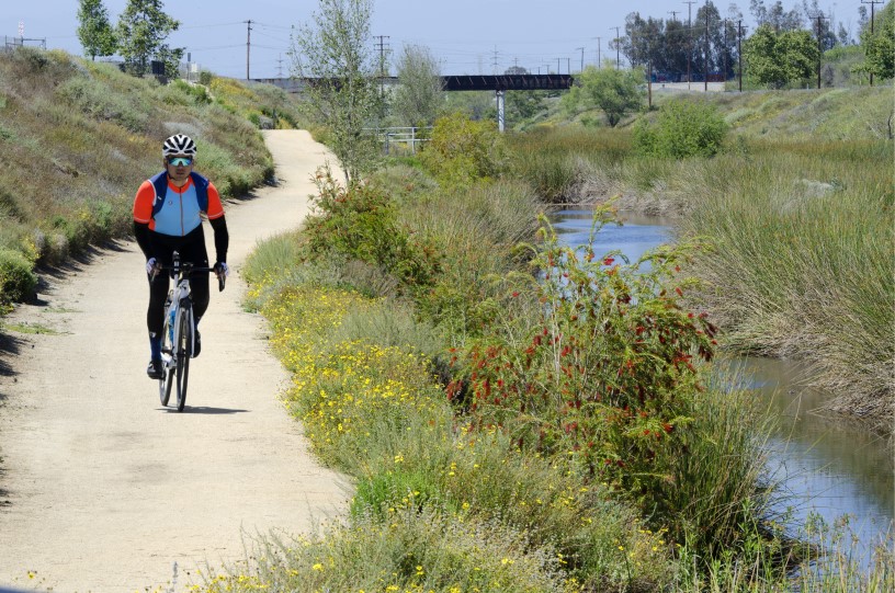 A thumbnail of a person riding a bike down a dirt path next to a creek with vegetation and flowers that provides more information about the topic Water quality and supplies